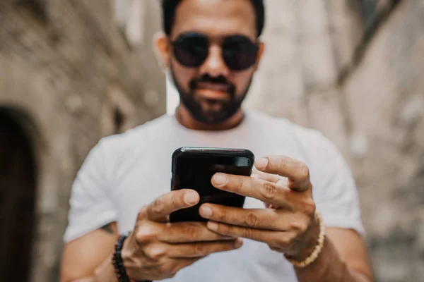 Jovem homem profissional urbano usando telefone inteligente. Hipster colega de trabalho segurando smartphone móvel usando mensagens SMS aplicativo usando óculos de sol — Fotografia de Stock