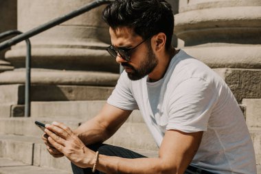 Yakışıklı sakallı İspanyol adam için dalga köpüğü hareket eden smartphone kullanarak Internet, web yapma çağrısı ve seyir dijital şehir haritası. Seyahat elektronik cihaz kullanarak erkek