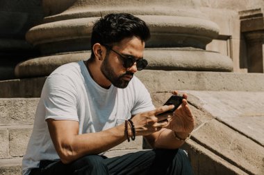 Yakışıklı sakallı İspanyol adam için dalga köpüğü hareket eden smartphone kullanarak Internet, web yapma çağrısı ve seyir dijital şehir haritası. Seyahat elektronik cihaz kullanarak erkek