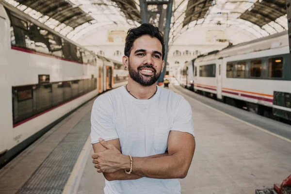 Happy Traveler male discover a big europe city, travel and active lifestyle concept.Bearded hispanic Tourist Man in white tshirt waiting his train on railway station.