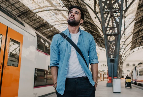 Happy Traveler male discover a big europe city, travel and active lifestyle concept.Bearded hispanic Tourist Man in blue shirt waiting his train on railway station.