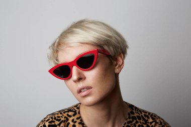 Genç güzel sevimli neşeli kız moda kırmızı güneş gözlüğü kameraya beyaz boş arka plan üzerinde seyir olarak portresi.