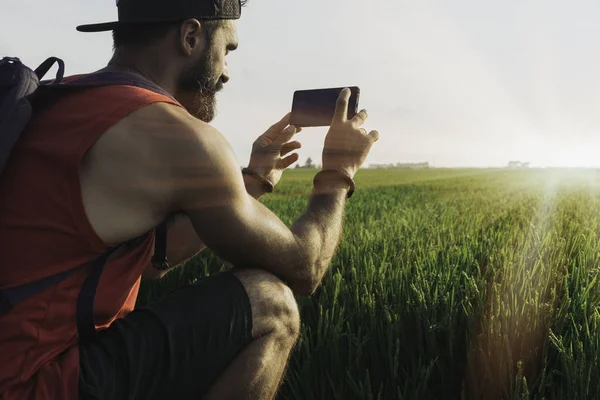 Sakallı adam modeli siyah kap ve üstünde hareket eden telefon fotoğraf yapma tshirt giyiyor. Günbatımı yeşil pirinç alanları sahne arka planda. Güneş ışığı görsel efektler.