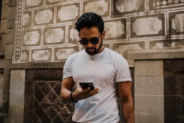 Young urban male professional using smart phone. Hipster coworker holding mobile smartphone using app texting sms message wearing sunglasses