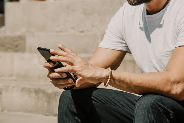 年轻的城市男性使用智能手机。hipster 拿着移动智能手机使用应用程序短信短信消息戴着太阳镜。裁剪. — 图库照片