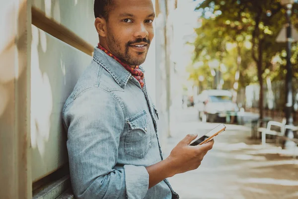 Africano hipster segurando smartphone navegando na internet e verificando feed de notícias em mídias sociais.Homem usando telefone celular — Fotografia de Stock