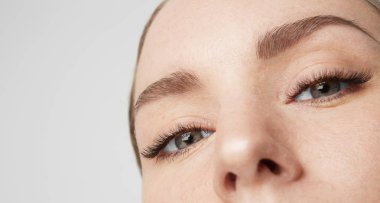 Yakın çekim portre güzellik kadın modeliyle büyük mavi gözleri ve karanlık kaşları kameraya bakıyor. Işık çıplak makyaj, gri studio arka plan ile model.