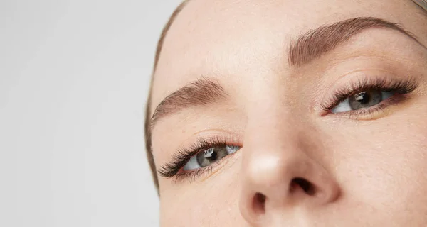 Nahaufnahme Porträt Schönheit weibliches Modell mit großen blauen Augen und dunklen Augenbrauen Blick auf camera.model mit hellem Nude-Make-up, grauer Studiohintergrund. — Stockfoto