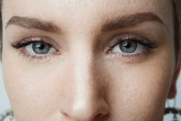 Close-up portret kobiety uroda duże niebieskie oczy i ciemne brwi, patrząc na kamery. Model z lekki makijaż Nagie, szare tło studio. — Zdjęcie stockowe