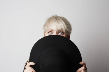 Moda portre genç güzel şık kadının beyaz boş arka plan üzerinde siyah şapka saklanıyor.