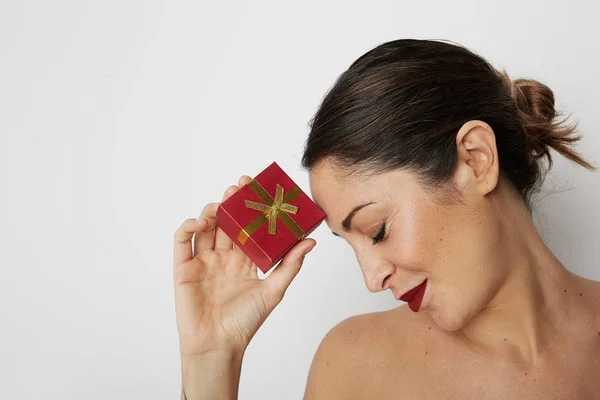 Gyönyörű barna nő tartja kezében piros ajándék doboz felett fehér üres háttér sötét hajjal. — Stock Fotó
