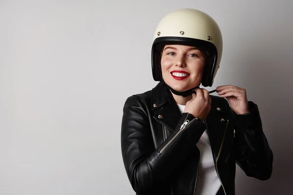 Chica feliz vistiendo chaqueta de cuero negro y casco moto sonriendo sobre fondo blanco. Concepto de moda, glamour y moto . Fotos de stock