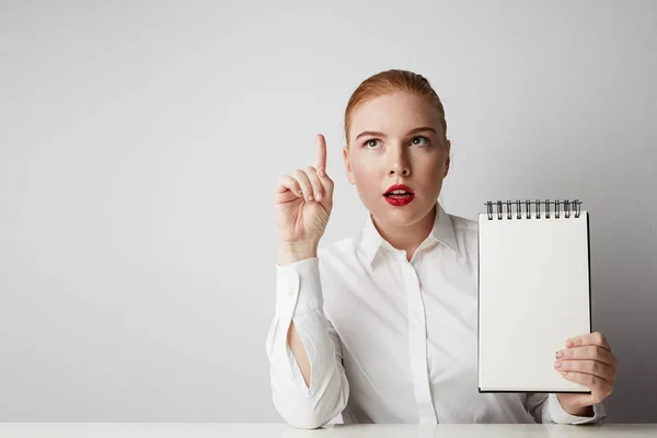 Retrato de mujer pelirroja de moda posando en camisa sosteniendo bloc de notas vacío sobre fondo blanco . Fotos de stock libres de derechos