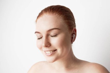 Romantik gülümseme ve kapalı gözler kulakta kablosuz kulaklık ile müzik arka plan üzerinde büyüleyici Kızıl saçlı kadın portresi.