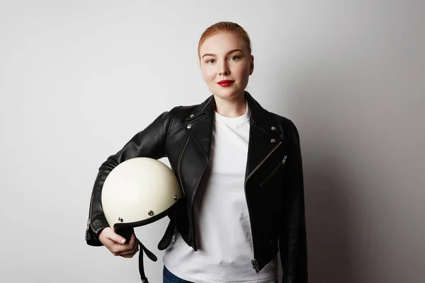 Handsome woman wearing black leather jacket holding white moto helmet over background. Fashion, glamour and moto wear concept. — Stock Photo, Image