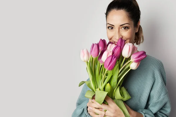 Portrait of a cheerful young woman holding colorful tulips bouquet isolated over gray background — Stock Photo, Image