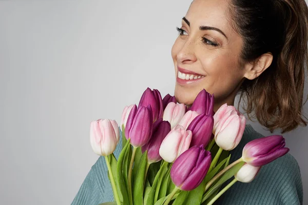 Closeup portrait of a smiling young woman holding colored tulips bouquet isolated over gray background — Stock Photo, Image
