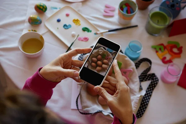 Happy easter decoration. Woman hands holding smartphone and making photo of colorful easter eggs on the table.