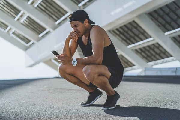 Ajuste muscular confiado modelo deportivo velocista descansando después de su entrenamiento y el uso de teléfono móvil para comprobar sus resultados . —  Fotos de Stock