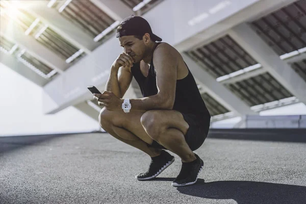 Atractivo modelo deportivo musculoso sprinter descansando después de su entrenamiento y utilizando el teléfono móvil para comprobar sus resultados . —  Fotos de Stock