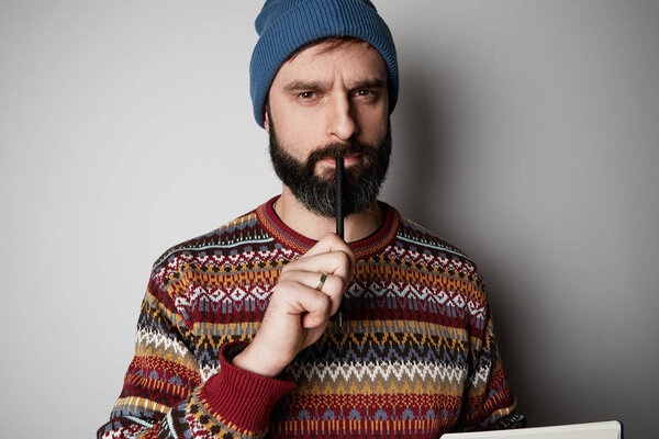 Young thoughtful bearded man in blue beanie thinking about test over empty background.