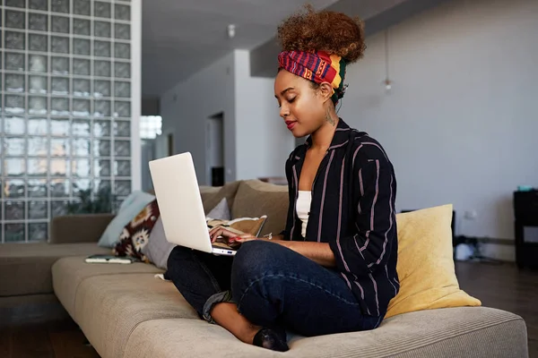 Young american african female blogger working remotely on digital netbook with internet text. African woman copywriter typing article for website on keyboard of modern laptop computer at home
