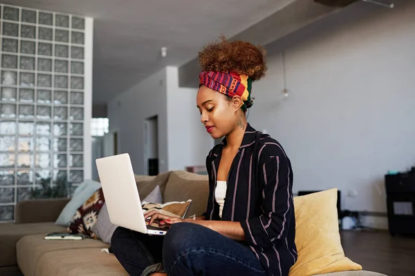 Jovem blogueira africana americana trabalhando remotamente em netbook digital com texto na internet. Mulher africana copywriter artigo de digitação para o site no teclado do computador portátil moderno em casa — Fotografia de Stock