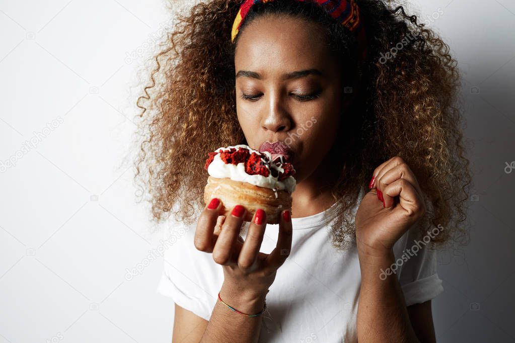 Black american african woman making a mess eating a huge fancy dessert over white background