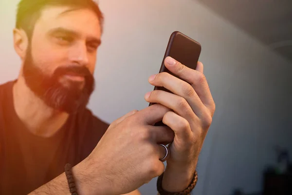 Уверенный бородатый мужчина, использующий мобильный смартфон в офисе. Размытое прошлое. Вспышка . — стоковое фото