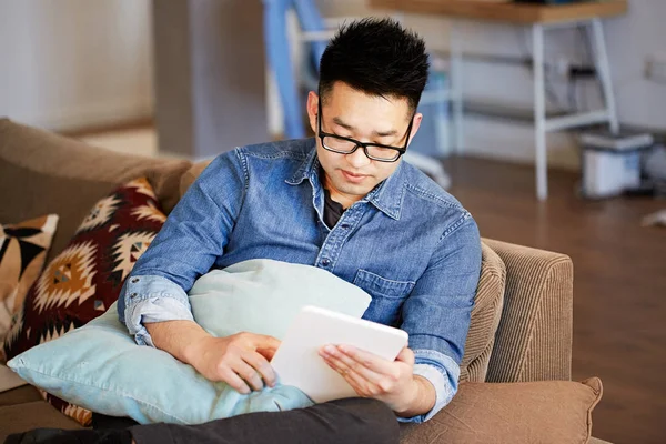 Jeune homme asiatique utilisant sa tablette électronique tout en se relaxant sur le canapé confort au studio de coworking — Photo