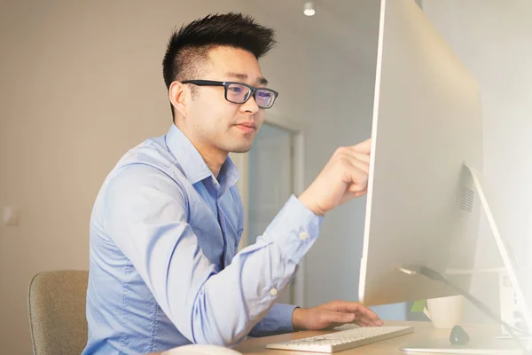 Jovem asiático cripto blockchain profissional vestindo camisa e óculos trabalhando enquanto sentado na frente do computador desktop em co-working escritório . — Fotografia de Stock