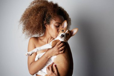 Beyaz arka planda köpek yavrusu kucaklayan güzel siyah amerikalı afrikalı kız. Beyaz arka plan üzerinde köpek ile ürpertici beyaz çekici kadın Stüdyo portresi.