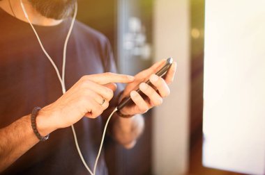 Evde mutlu olan Smartphone sosyal ağlar kontrol, kulaklıkları rahat gri t-shirt dinleme müzik giyen sakallı adam