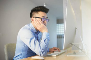 Genç Asya adam programcı giyen gömlek ve gözlük çalışma sırasında masaüstü bilgisayar önünde oturan içinde çalışan ofis.