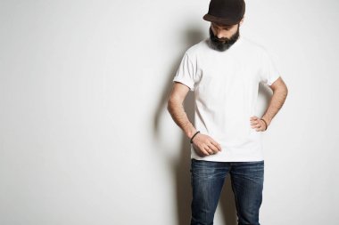 Beyaz boş t-shirt giyen sakallı kaslı adam modeli ve beyaz arka planda rahat kentsel tarzında logonuz veya tasarım için alan ile siyah bir snapbuck kap.