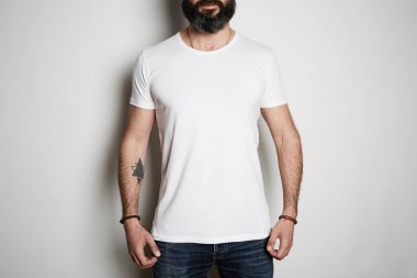 Çekici acımasız dövmeli sakallı adam mavi kot ve boş gri t-shirt prim yaz pamuk, beyaz arka plan mockup üzerinde pozlar