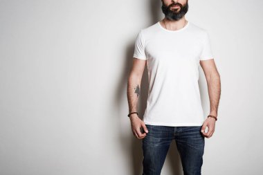 Sakallı kaslı adam model beyaz arka planda rahat kentsel tarzında logonuzu veya tasarım için boşluk ile beyaz boş t-shirt giyiyor. Stüdyo çekimi