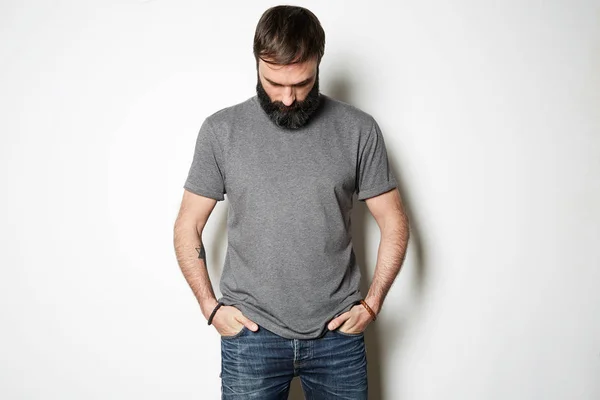 Bearded man in blank gray t-shirt, white wall on background — Stock Photo, Image