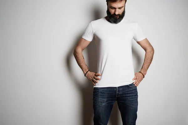 Young brutal tattooed bearded guy poses in blue jeans and blank white t-shirt premium summer cotton, on white background. — Stock Photo, Image