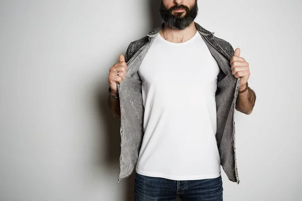 Positivo brutal barbudo masculino modelo poses no preto jeans camisa e branco branco t-shirt premium verão algodão, no fundo branco . — Fotografia de Stock