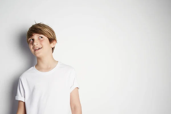 Niño guapo en camiseta blanca posando frente a una pared blanca y vacía. Retrato de niño masculino de moda. Niño sonriente posando, pared en blanco en el fondo. Concepto de estilo y moda infantil . — Foto de Stock