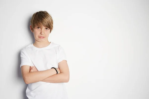 Upset young boy in white T-shirt posing in front of white empty wall. Portrait of fashionable male child. Smiling boy posing, blank wall on background. Concept of children style and fashion — Stock Photo, Image