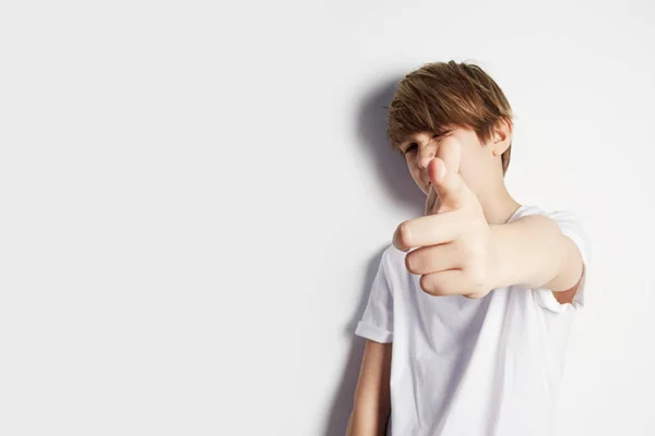 Atractivo joven en camiseta blanca posando frente a una pared blanca vacía. Retrato de niño masculino de moda. Niño sonriente posando, pared en blanco en el fondo. Concepto de estilo y moda infantil . — Foto de Stock