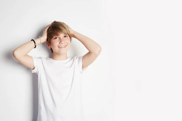 Rapaz sorridente de t-shirt branca a posar em frente à parede branca vazia. Retrato de criança masculina na moda. Rapaz sorridente posando, parede em branco no fundo. Conceito de estilo infantil e moda — Fotografia de Stock