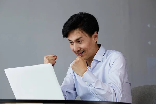 Feliz animado jovem asiático homem com laptop em casa sentado na mesa — Fotografia de Stock