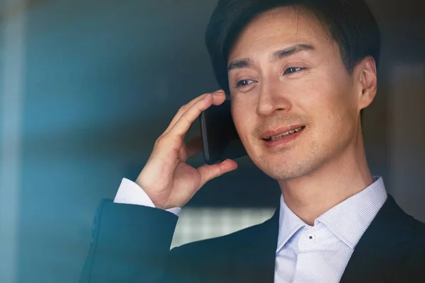 Confiante asiático empresário falando no telefone celular no fundo embaçado — Fotografia de Stock