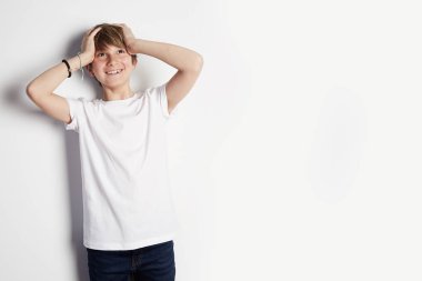 Çocuk stil ve moda kavramı. Beyaz boş duvar arka plan önünde poz beyaz t-shirt gülümseyen genç çocuk. Mockup.