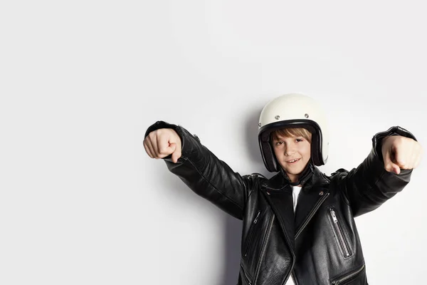 Young cute cheerful teen boy in black leather jacket and white moto helmet pretending to ride a motorcycle over on white background. — Stock Photo, Image