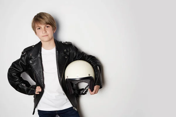 Portret van jonge knappe tiener Kid in zwart lederen jas en holding hand witte Moto helm glimlachend op witte achtergrond. — Stockfoto