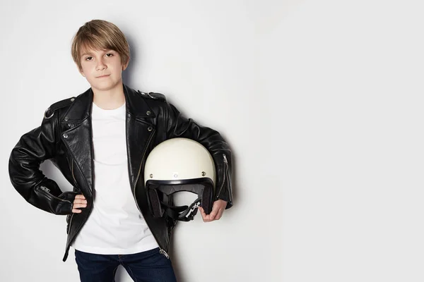 Retrato de Joven guapo adolescente en chaqueta de cuero negro y sosteniendo la mano casco moto blanco sonriendo sobre fondo blanco . — Foto de Stock